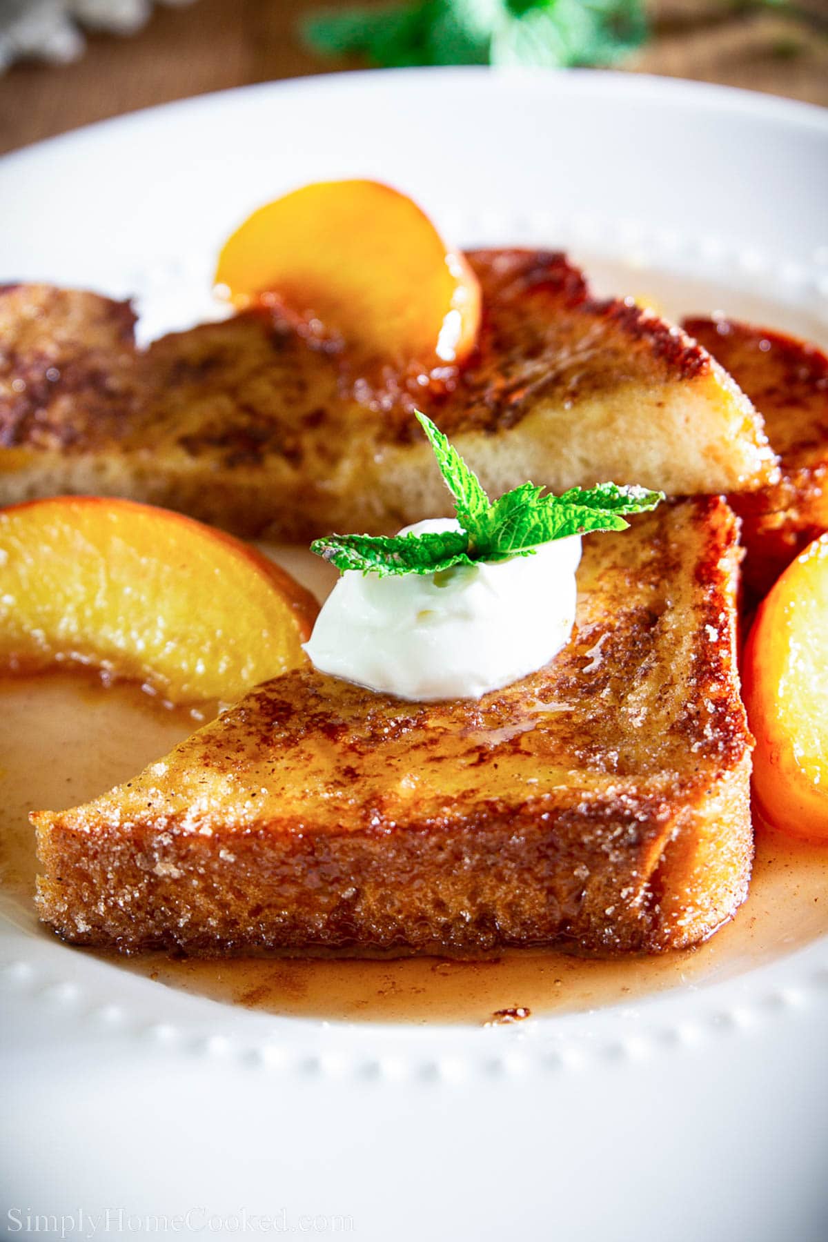 Cinnamon Peach French toast drizzled with caramelized rum and peach syrup. This easy recipe is topped with creme fraiche for the ultimate breakfast. #peachfrenchtoast #frenchtoast #peachsyrup #peachtaost #peachesandcream Peach French Toast topped with peach rum syrup, creme fraiche, and a spring of mint.