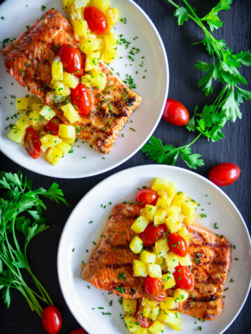 Pineapple Salmon on a plate with pineapple, cherry tomatoes, and chopped parsley on top.