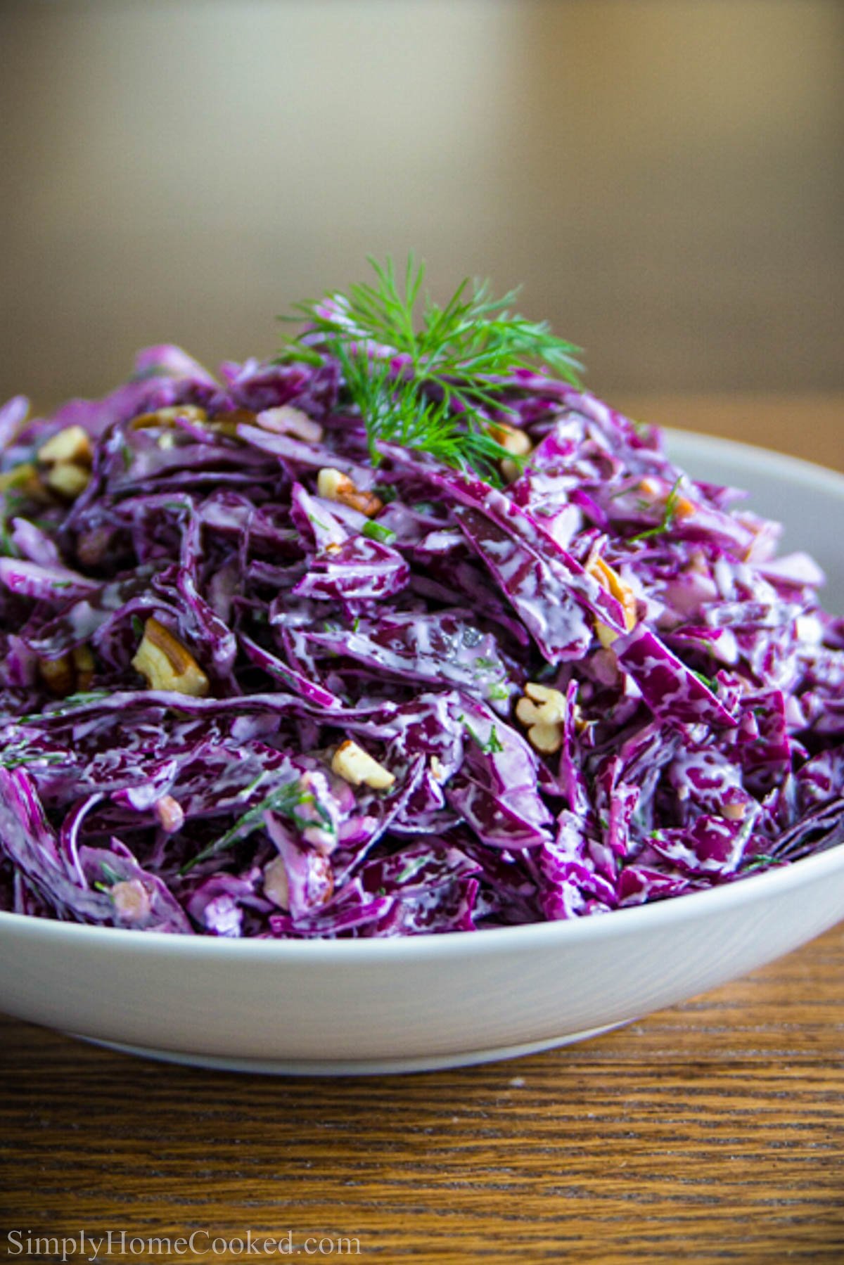Bowl of Purple Cabbage Salad topped with creamy dressing, fresh dill, and toasted pecans.