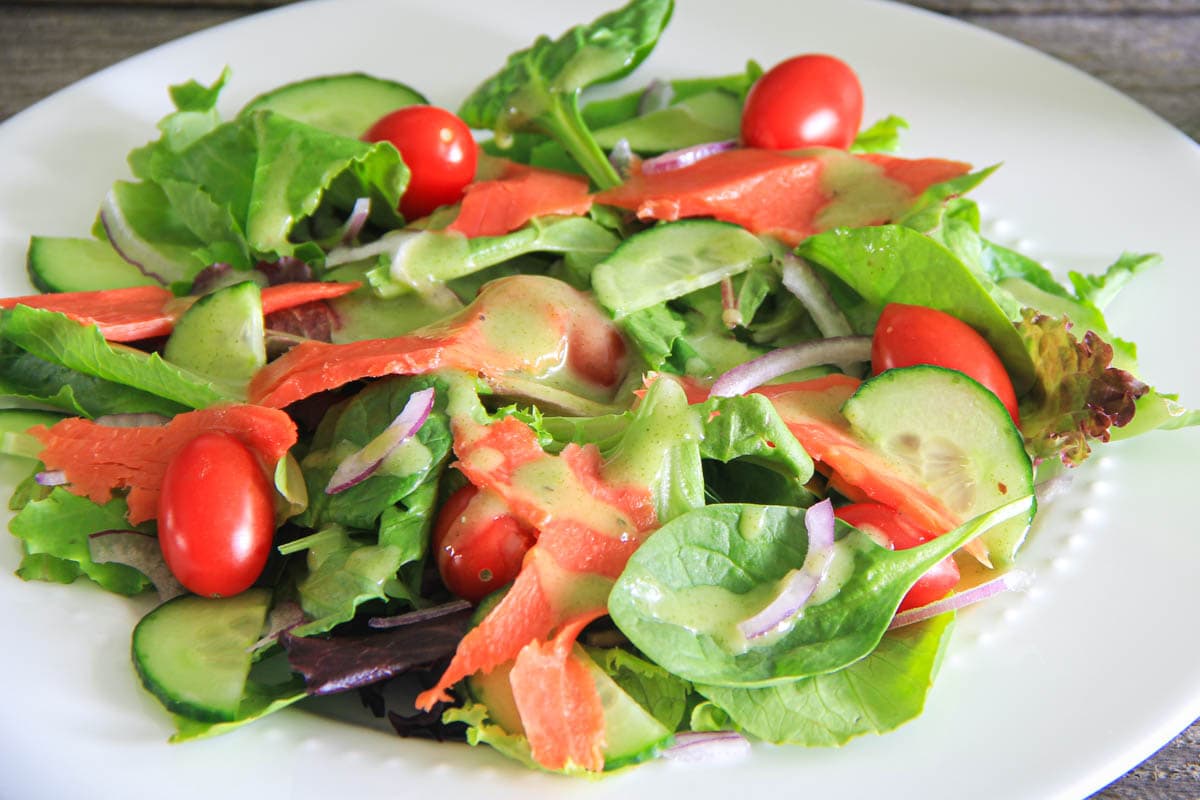 Smoked Salmon Salad on a white plate with tomatoes, cucumber, onion, and dressing.