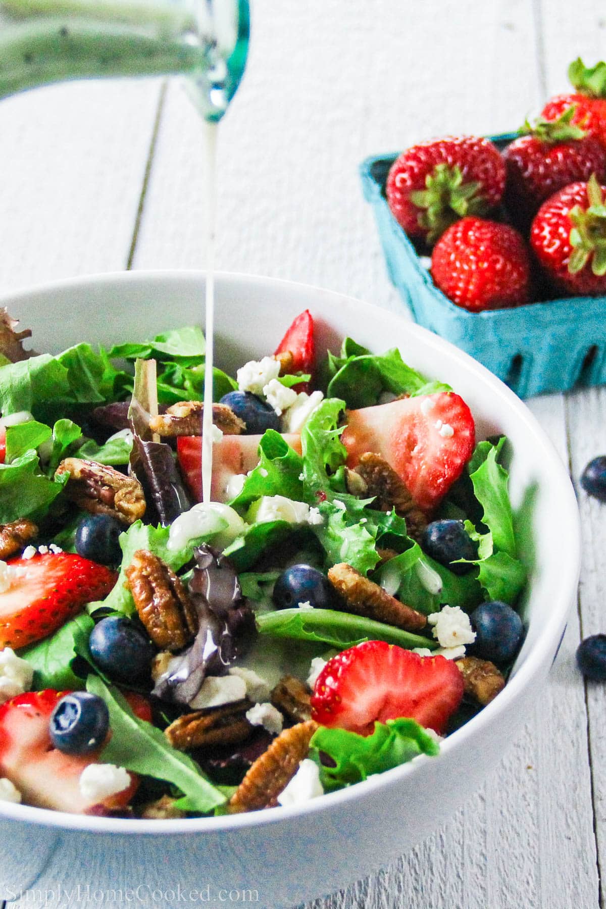 Dressing drizzling onto Strawberry Feta Spinach Salad with berries on the side.