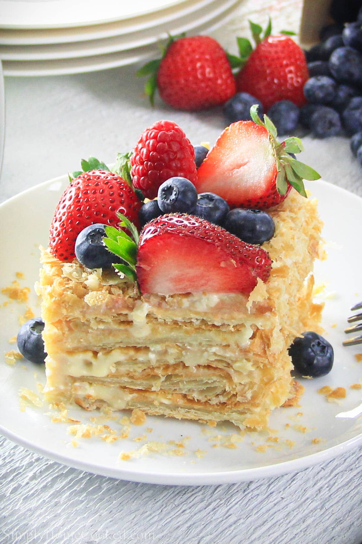 This is the easiest Napoleon cake recipe! Layered with a delicious custard cream and topped with fresh berries, your family will love it. #napoleoncake #russiannapoleon #napoleon #layeredcake #puffpastrycake Slice of Easy Napoleon Cake topped with fresh berries.
