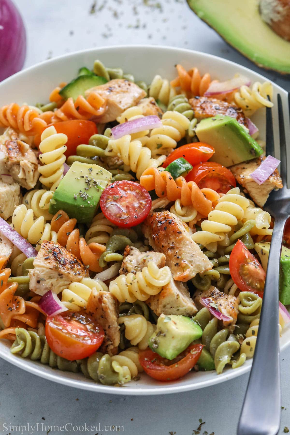 Chicken Pasta Salad with tomatoes, cucumber, avocado, rotini, and chicken in a bowl with a fork.