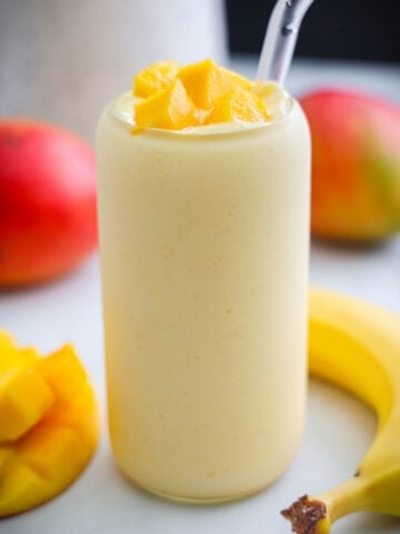 Mango Smoothie topped with mango chunks and with banana and mango nearby.