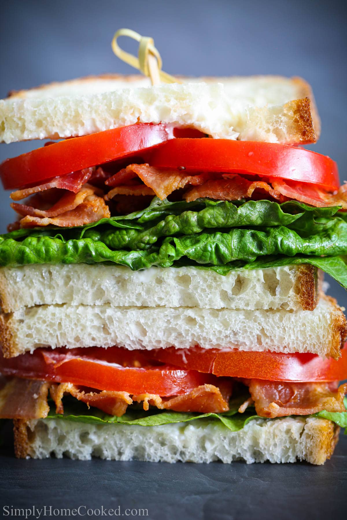 A BLT sandwich sliced and piled with bacon, lettuce, and tomato on white bread.