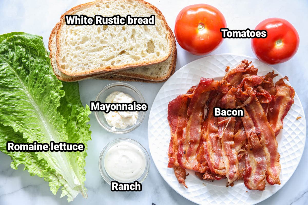 Ingredient for a BLT sandwich: romaine lettuce, white rustic bread, mayonnaise, ranch, bacon, and tomatoes.