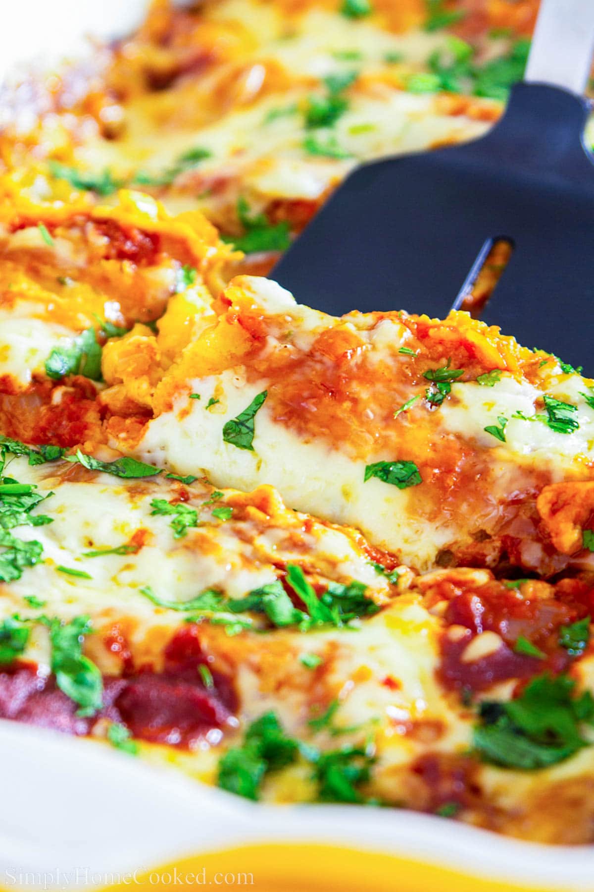 Chicken Enchiladas with Red Sauce being lifted out of the pan with a spatula.