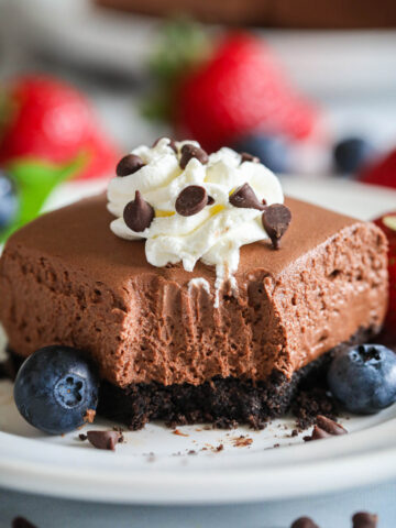 A No-bake Chocolate Cheesecake Bar missing a forkful and topped with whipped cream and chocolate chips.