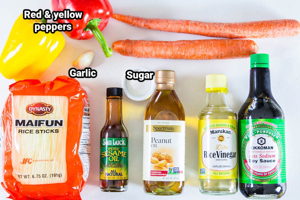 Ingredients for Sesame Noodle Salad: red and yellow bell peppers, carrots, rice noodles, garlic clove, sugar, peanut oil, sesame oil, rice vinegar, and soy sauce.
