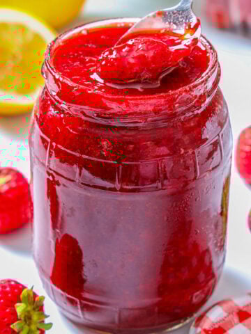 Jar of homemade 3-ingredient Strawberry Jam with a spoonful being lifted out.