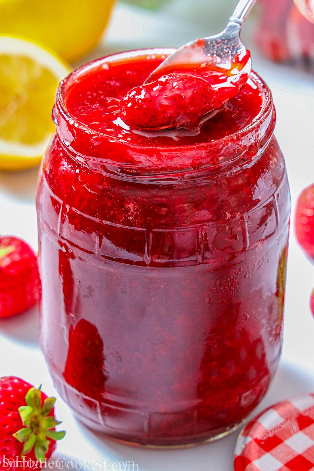 Jar of homemade 3-ingredient Strawberry Jam with a spoonful being lifted out.