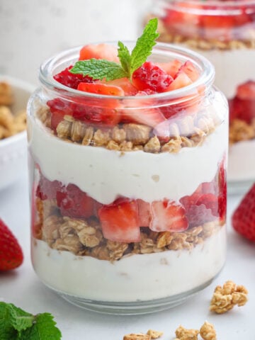 Strawberry Parfait in a jar layered with yogurt, granola, and strawberry pieces and topped with a mint leaf.