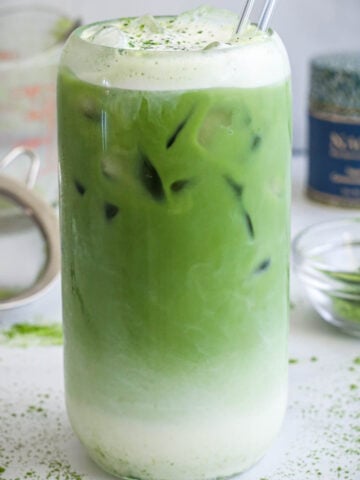 Iced Matcha Latte topped with cold foam in a glass with a straw.