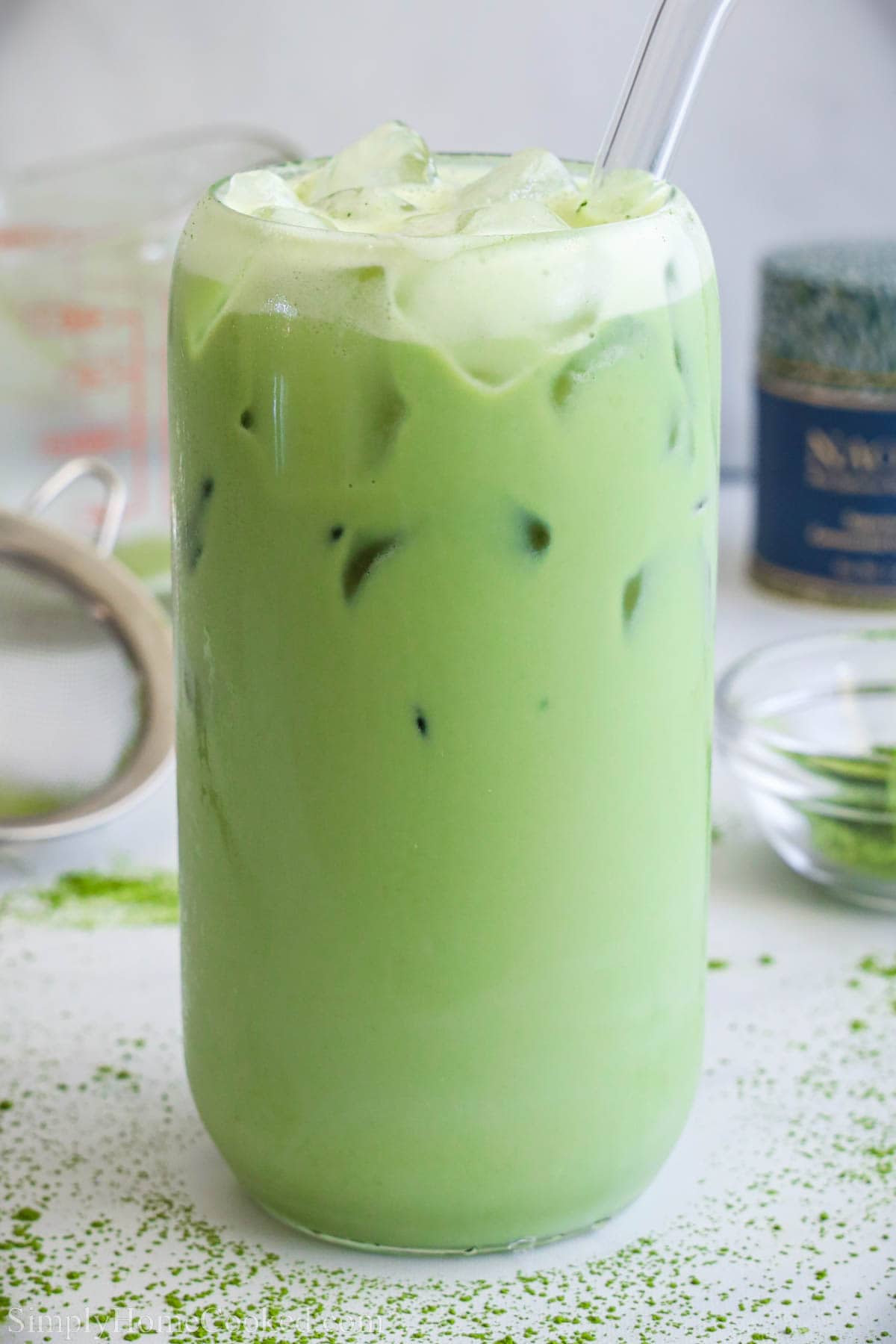 Iced Matcha Latte in a tall glass with a straw surrounded by a sprinkle of matcha powder.