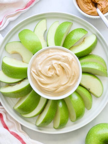Peanut Butter Yogurt Dip in the center of apple slices with peanut butter nearby.