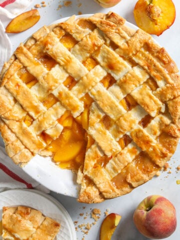 Perfect Peach Pie missing a piece surrounded by fresh peaches.