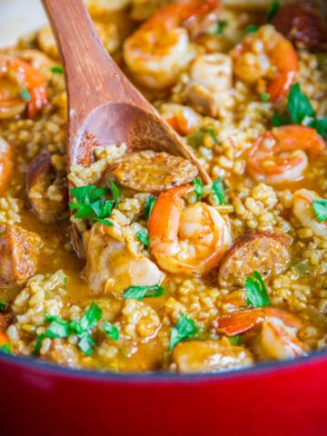 Wooden spoon dipping into a pot of Brown Rice Jambalaya.