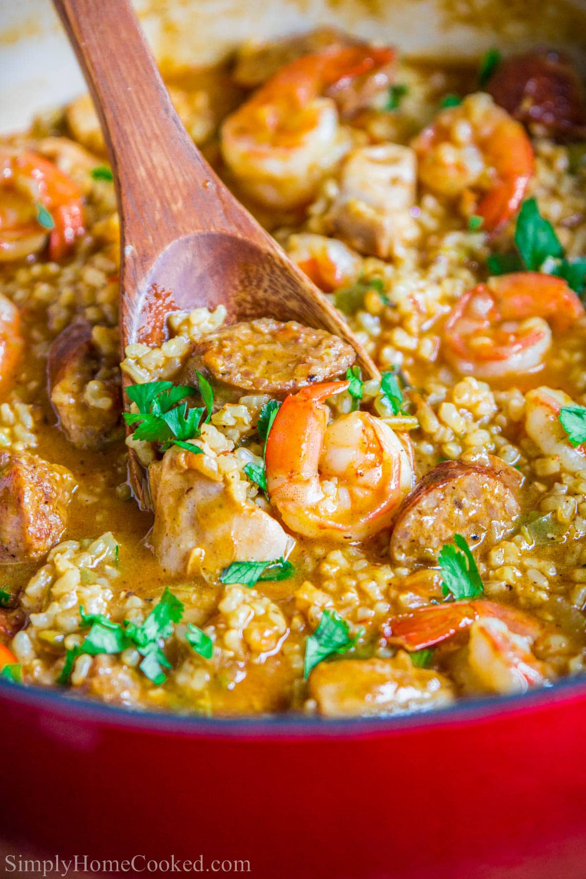 Wooden spoon dipping into a pot of Brown Rice Jambalaya.