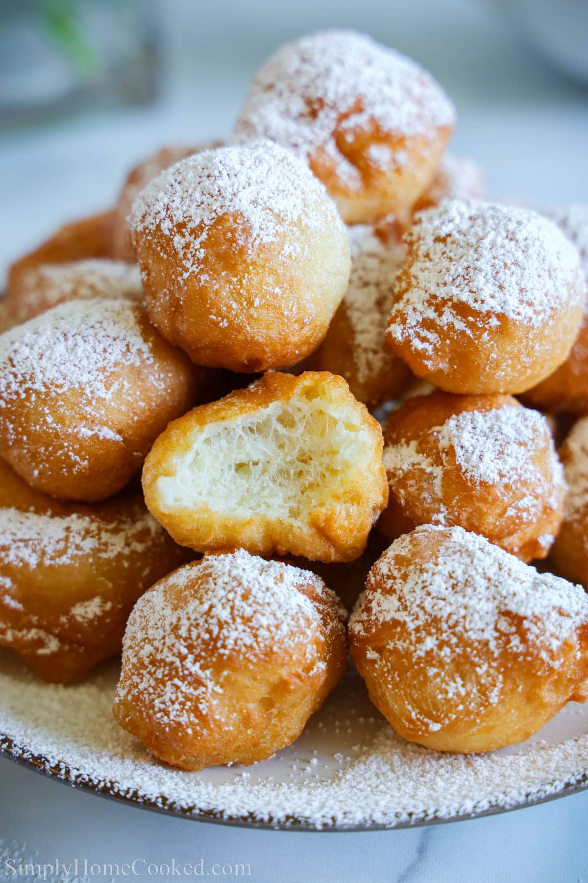 This Zeppole Recipe makes the most delicious sugar-topped fried dough. You have got to try these yummy Italian donuts! #zeppole #zeppoles #zeppolerecipe #Italiandonuts Close up of Zeppoles on a plate with powdered sugar on top.