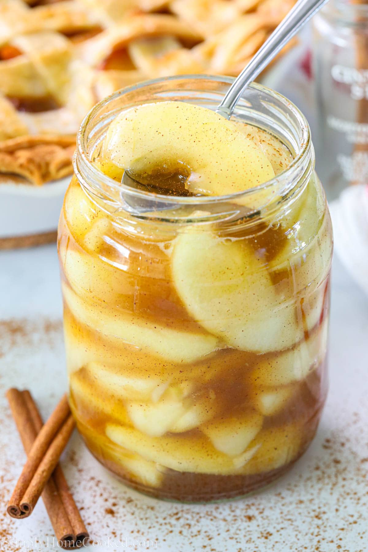 This Easy Apple Pie Filling is the perfect mix of sweet gooiness and tart apple. Serve it alongside ice cream, pastries, or in a homemade pie crust. #homemadeapplepie #homemadeapplepiefilling #applepiefilling #applepiefillingrecipe Homemade Apple Pie Filling in a mason jar with a spoon and cinnamon sticks nearby.