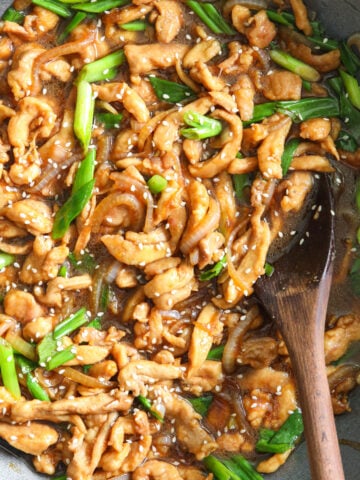 Mongolian Chicken in a wok with a wooden spoon.