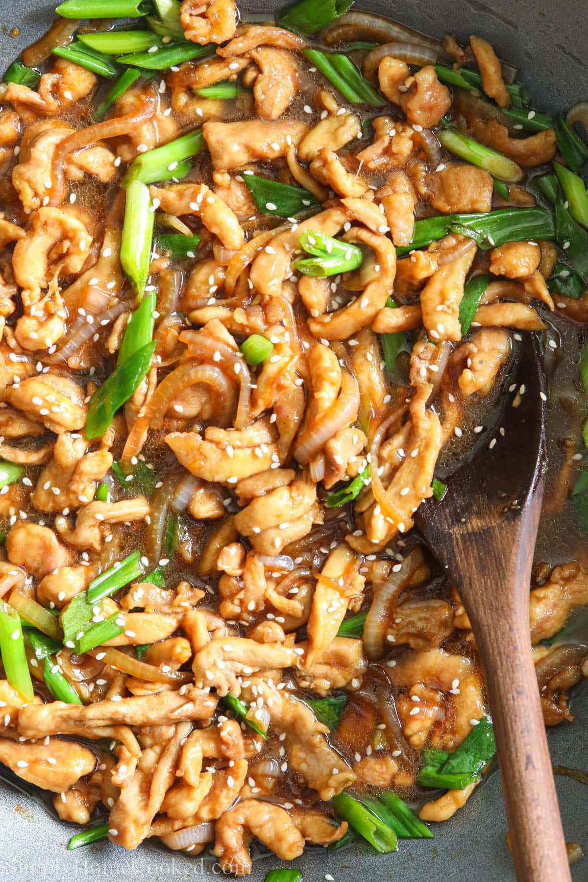 Mongolian Chicken in a wok with a wooden spoon.