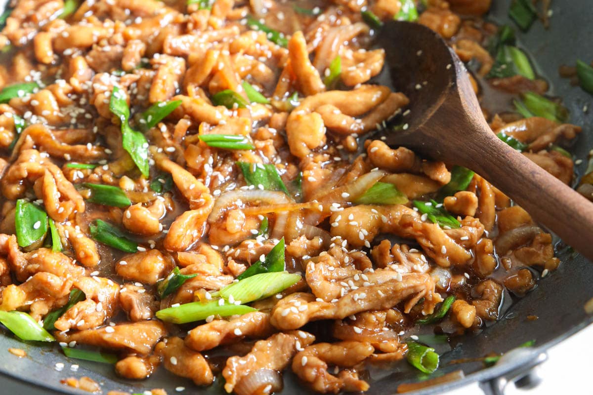 Wooden spoon stirring Mongolian Chicken in a wok.