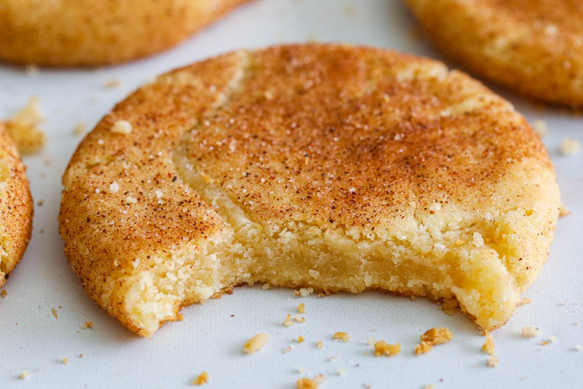 If you are making a cookie platter this holiday season, start with these Soft Snickerdoodle Cookies. They are cinnamon-sugar coated and taste amazing. #holidaycookierecipe #bestholidaycookies #bestholidaysnickerdoodlerecipe #bestcookieplatter Closeup of a Snickerdoodle Cookie missing a bite.