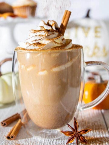 Pumpkin Spice Latte topped with whipped cream and being sprinkled with pumpkin pie spices.