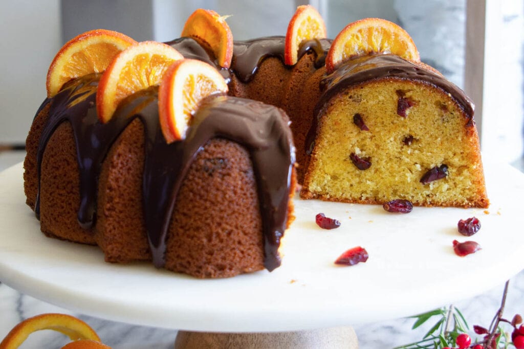 Cranberry Orange Bundt Cake topped with orange slices and ganache and sliced. 