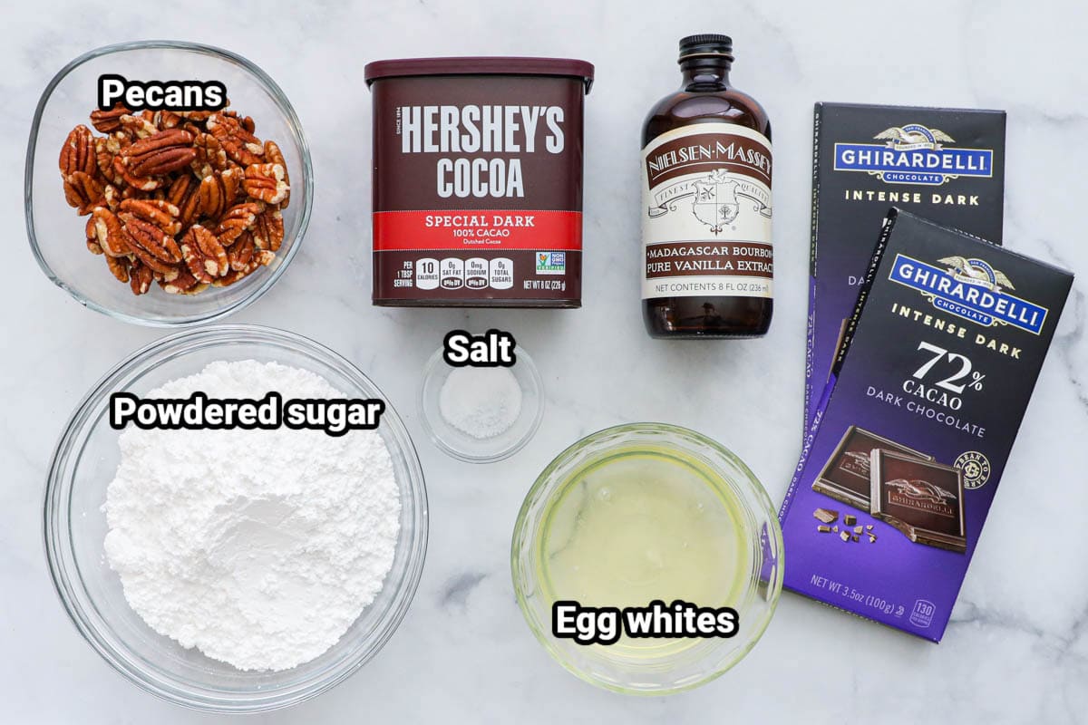Ingredients for Flourless Chocolate Cookies: powdered sugar, pecans, cocoa powder, vanilla extract, salt, egg whites, and dark chocolate. 