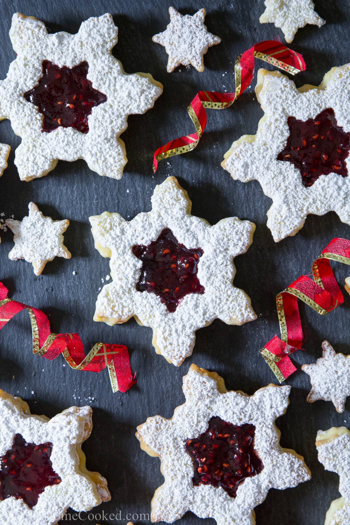 Homemade linzer cookies with raspberry jam are buttery, sweet, and tangy, making great holiday cookies for any party or just for the family. #linzercookies #raspberrylinzercookies #Christmascookies #linzercookieswithraspberryjam #bestholidaycookies Linzer Cookies with Raspberry Jam alongside ribbons.