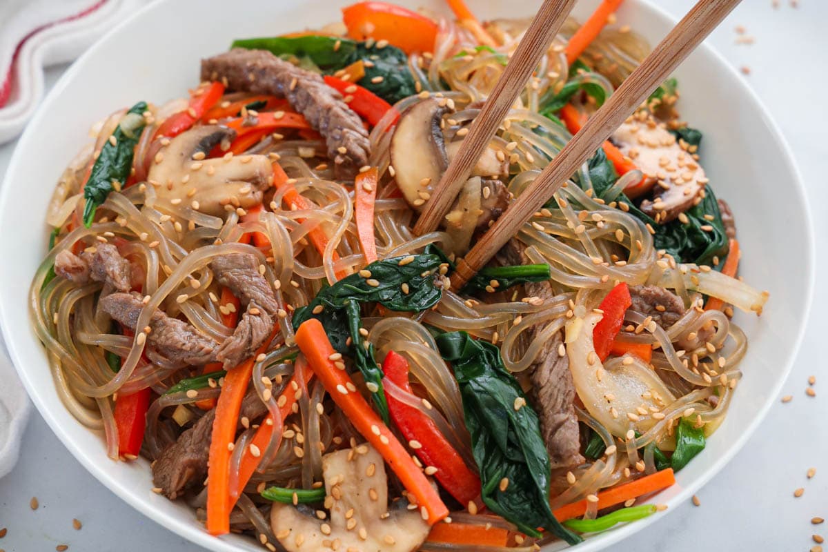 Easy Japchae in a white bowl with chopsticks. 