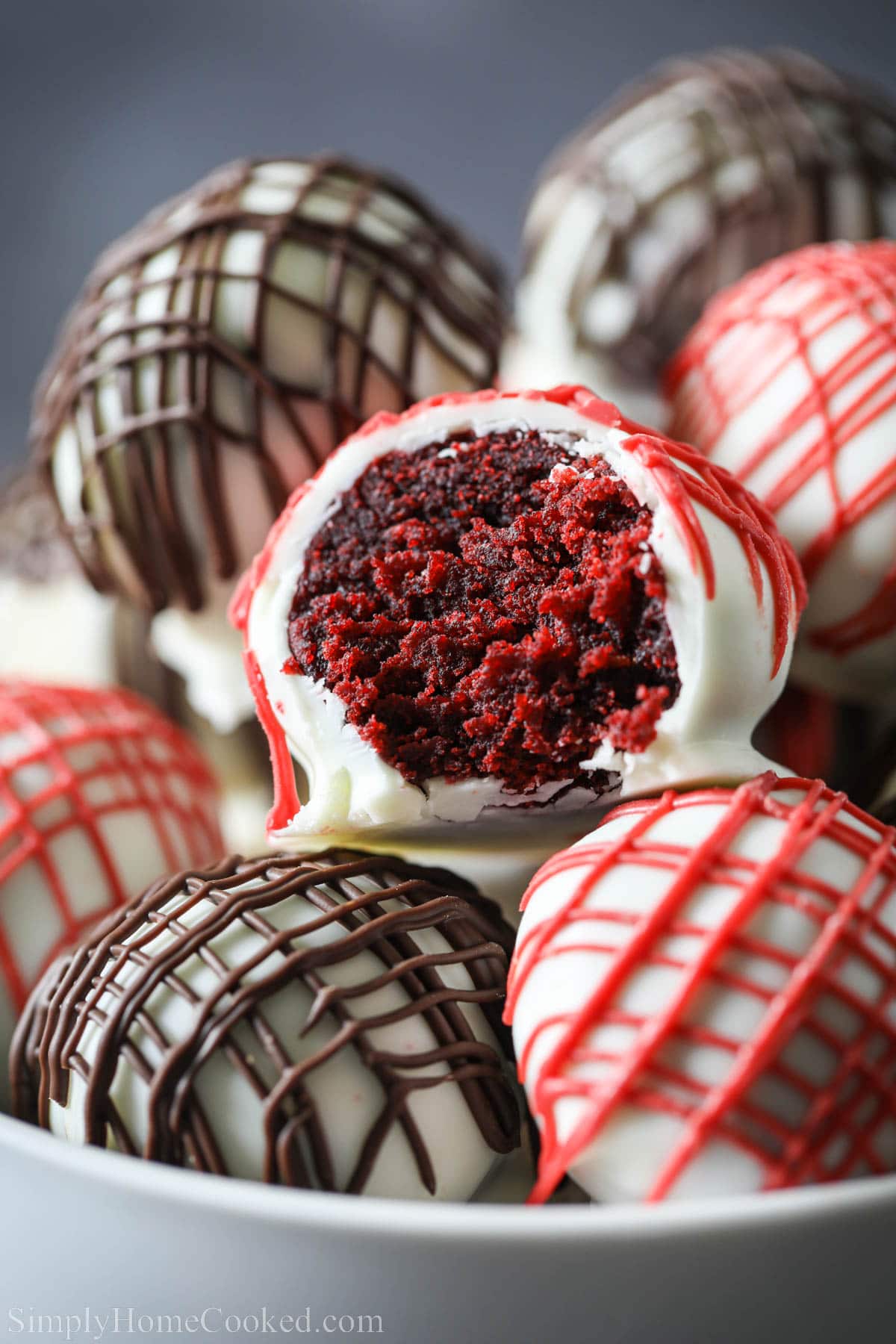 These Red Velvet Cake balls are so yummy. They have a soft red velvet inside and a hard candy coating on the outside. #dessert #valentinesdaydessert #redandwhitecakepops #valentinesdayrecipe Red Velvet Cake Balls covered in white chocolate candy melt and drizzled with red and chocolate.