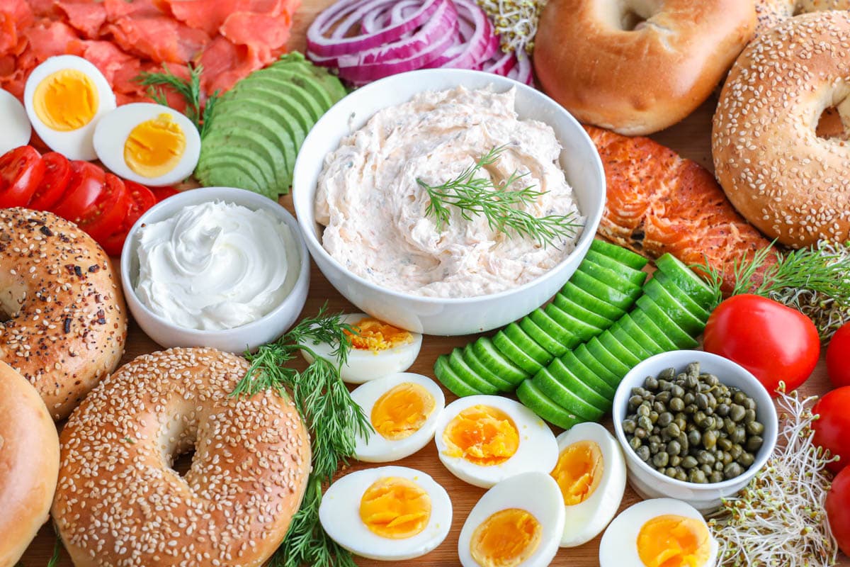 Bagels, cream cheese, smoked salmon spread, hard boiled eggs, cucumber, tomato, and avocado on a Bagel Board.
