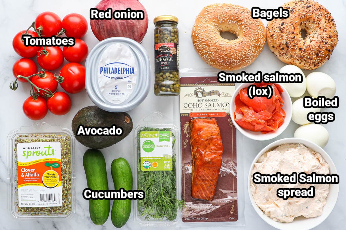 Ingredients for Bagel Board: tomatoes, red onion, capers, cream cheese, avocado, cucumber, alfalfa, smoked salmon, lox, bagels, boiled eggs, and smoked salmon spread.