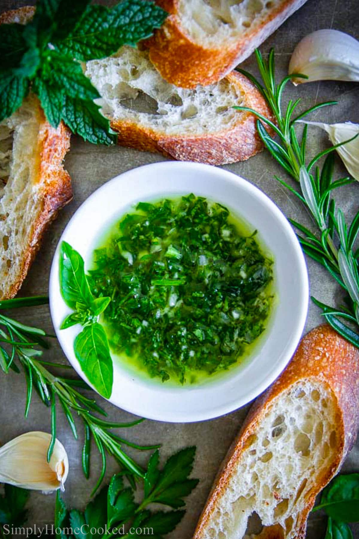 The best dipping oil for just about any bread recipe. Its bursting with herb and garlic flavor. #breaddip #dipingoil #herboil #breadoil #garlicherbdip Bowl of Bread Dipping Oil with fresh rosemary and bread nearby.