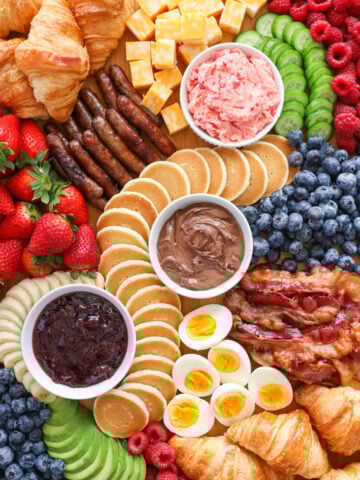 A Breakfast Charcuterie Board with spreads, pastries, fruits, eggs, bacon, and sausage.