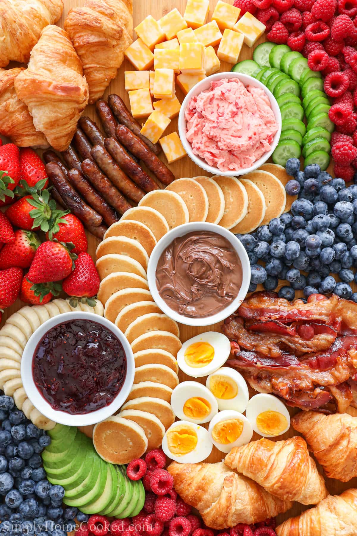 A Breakfast Charcuterie Board with spreads, pastries, fruits, eggs, bacon, and sausage.