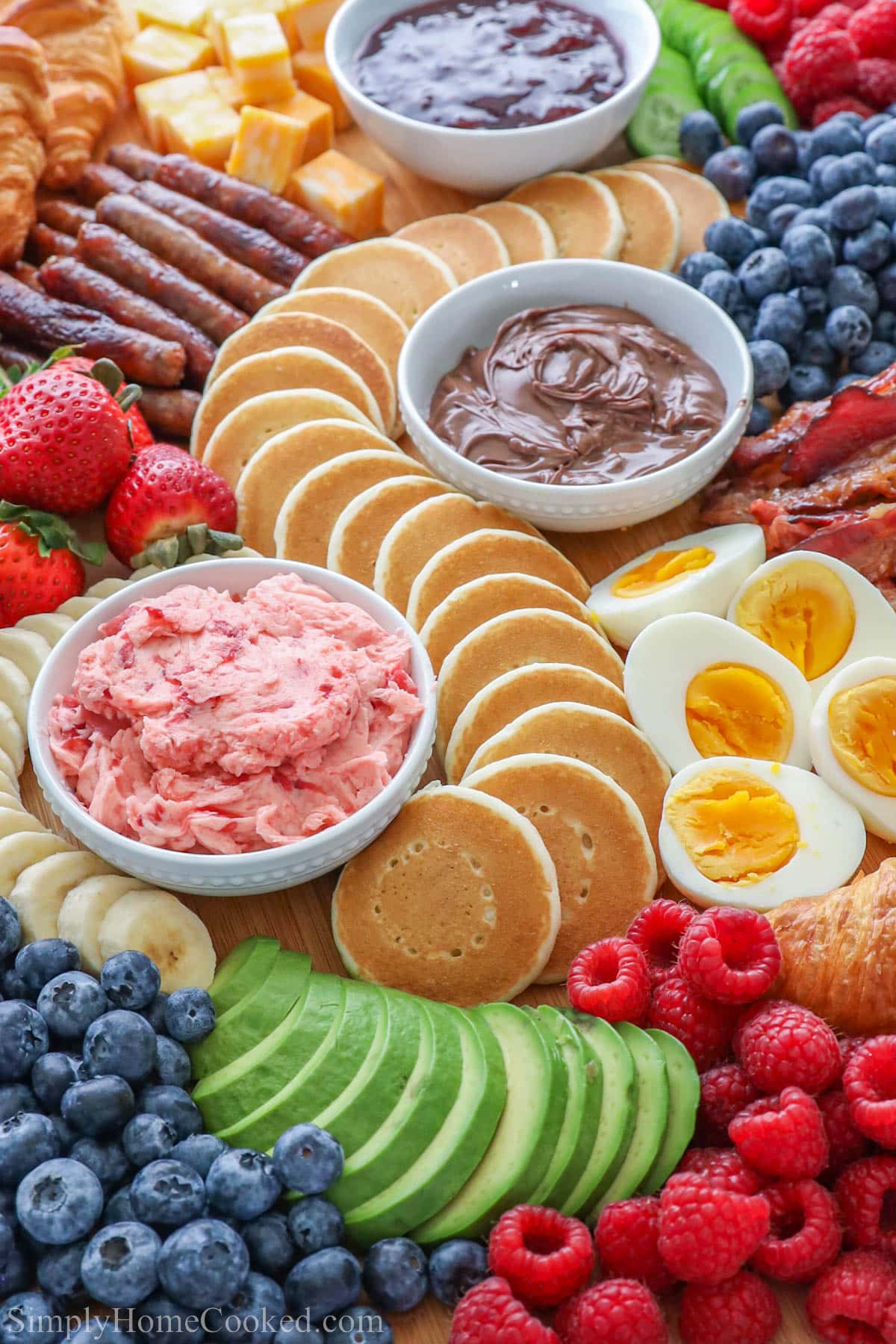 Breakfast Charcuterie Board filled with pancakes, eggs, meats, berries, strawberry butter, and Nutella.