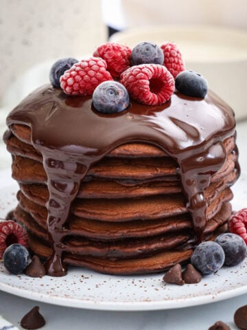 Stack of Chocolate Pancakes topped with chocolate ganache and berries.
