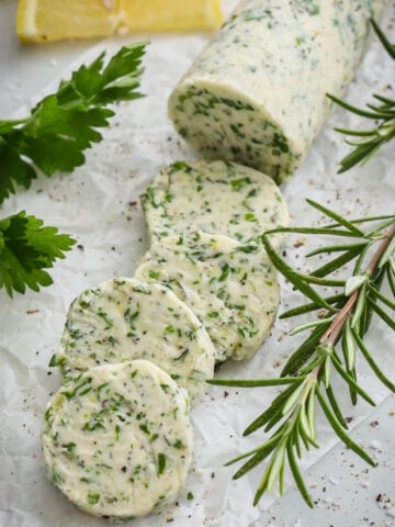 Compound Butter for Steak sliced with parsley and rosemary nearby.
