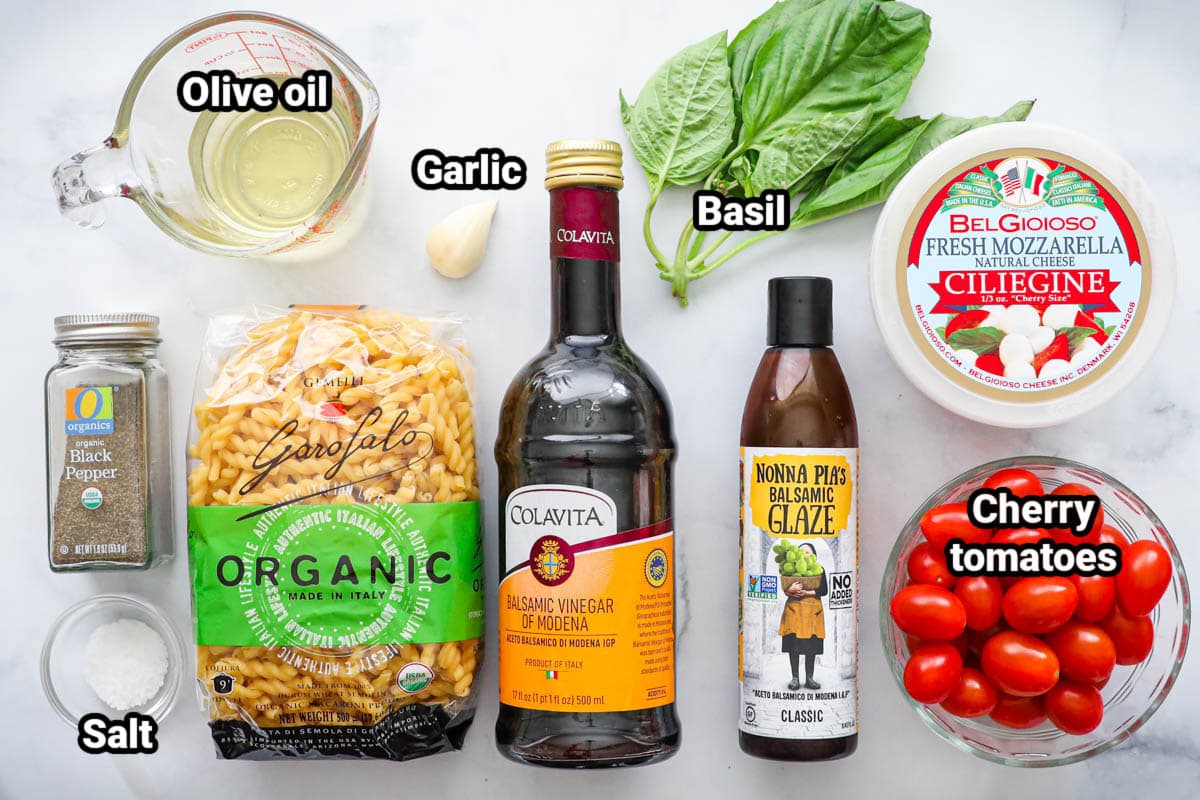 Ingredients for Caprese Pasta Salad: cherry tomatoes, fresh mozzarella, basil, balsamic glaze, balsamic vinegar, garlic, pasta, salt, black pepper, and olive oil.
