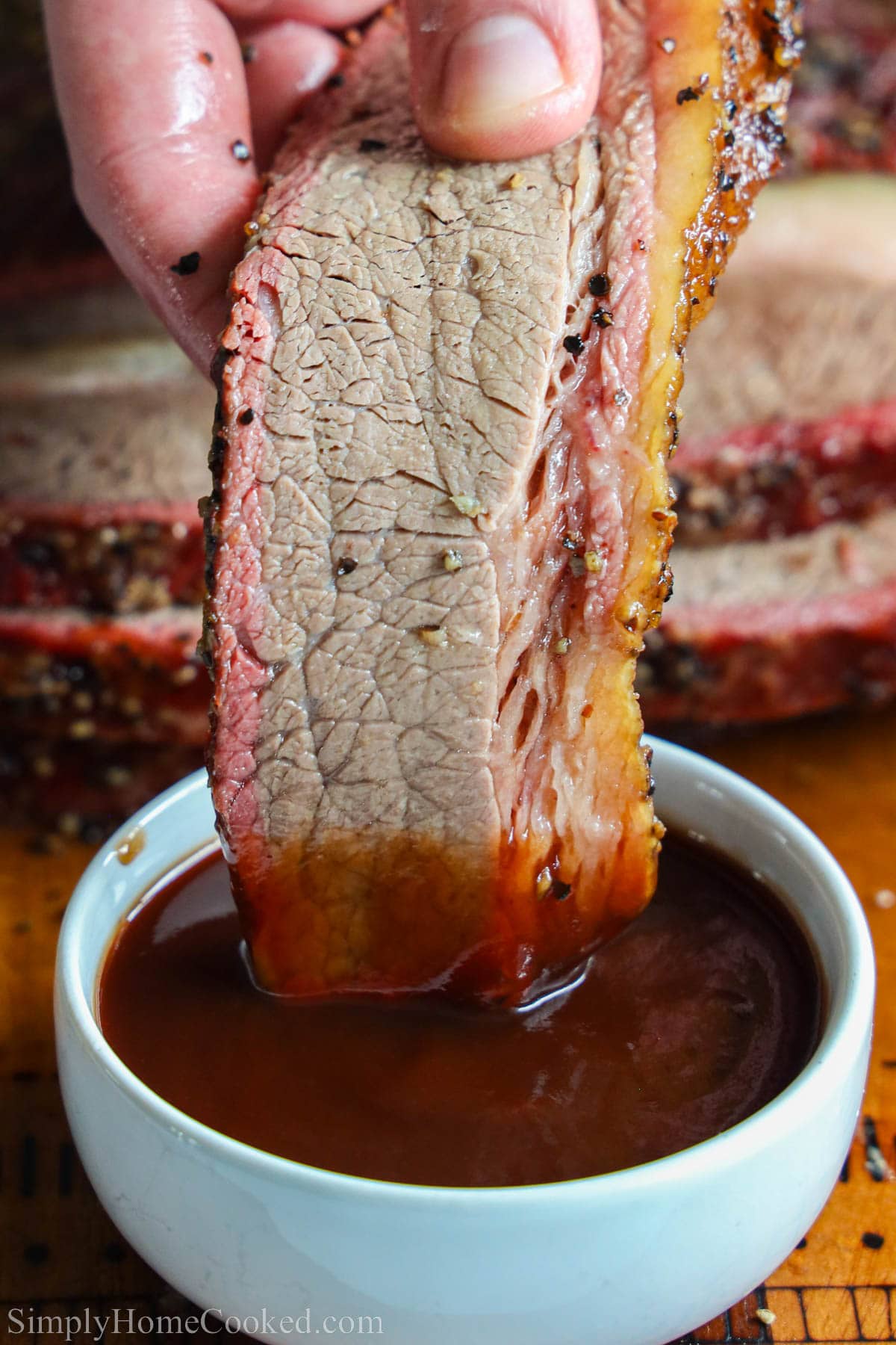 Dipping piece of Smoked Beef Brisket into barbecue sauce.