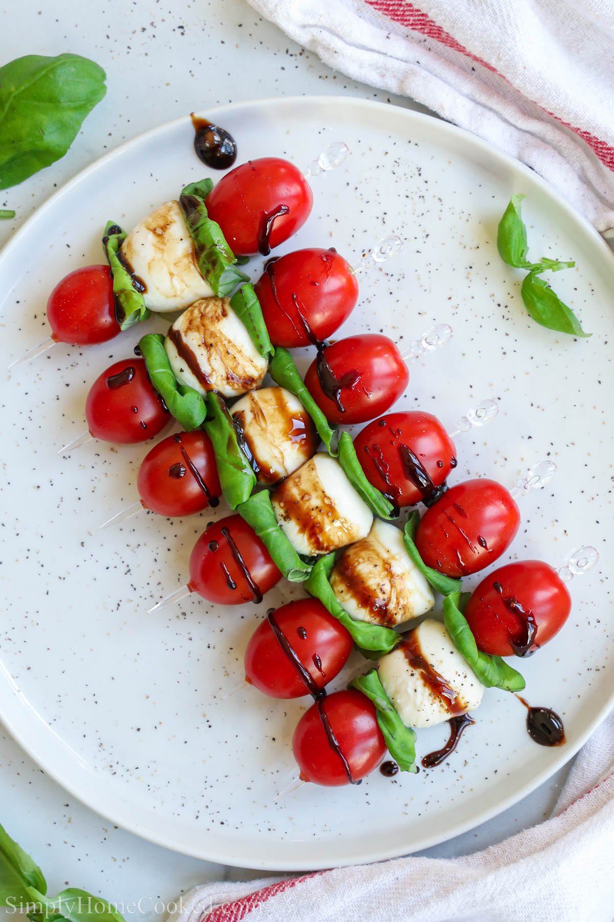Caprese Skewers lined up on a plate and drizzled with balsamic glaze. 