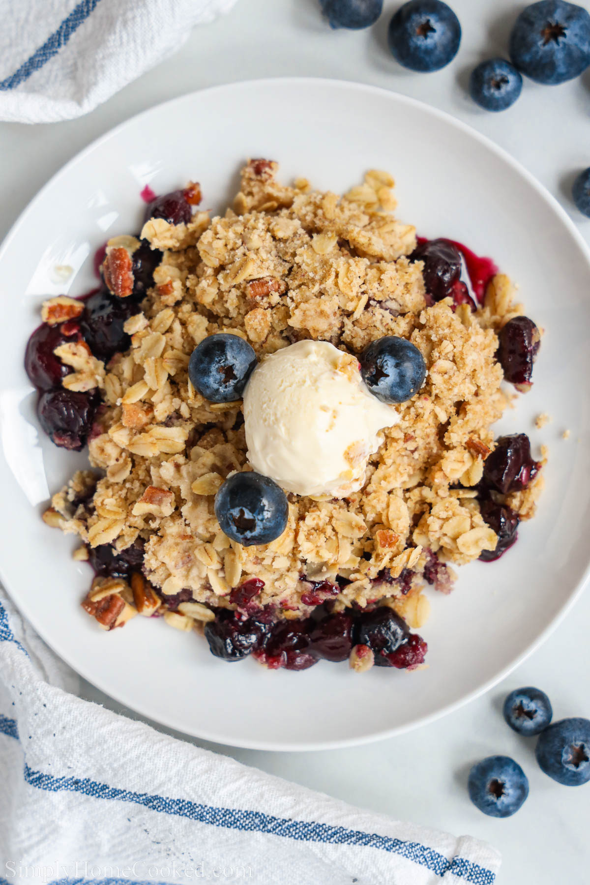 Overview of Blueberry Crisp topped with fresh blueberries and vanilla ice cream. 