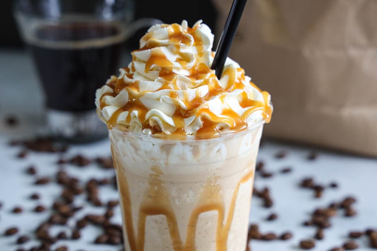 Caramel Frappuccino with a straw and coffee beans in the background.