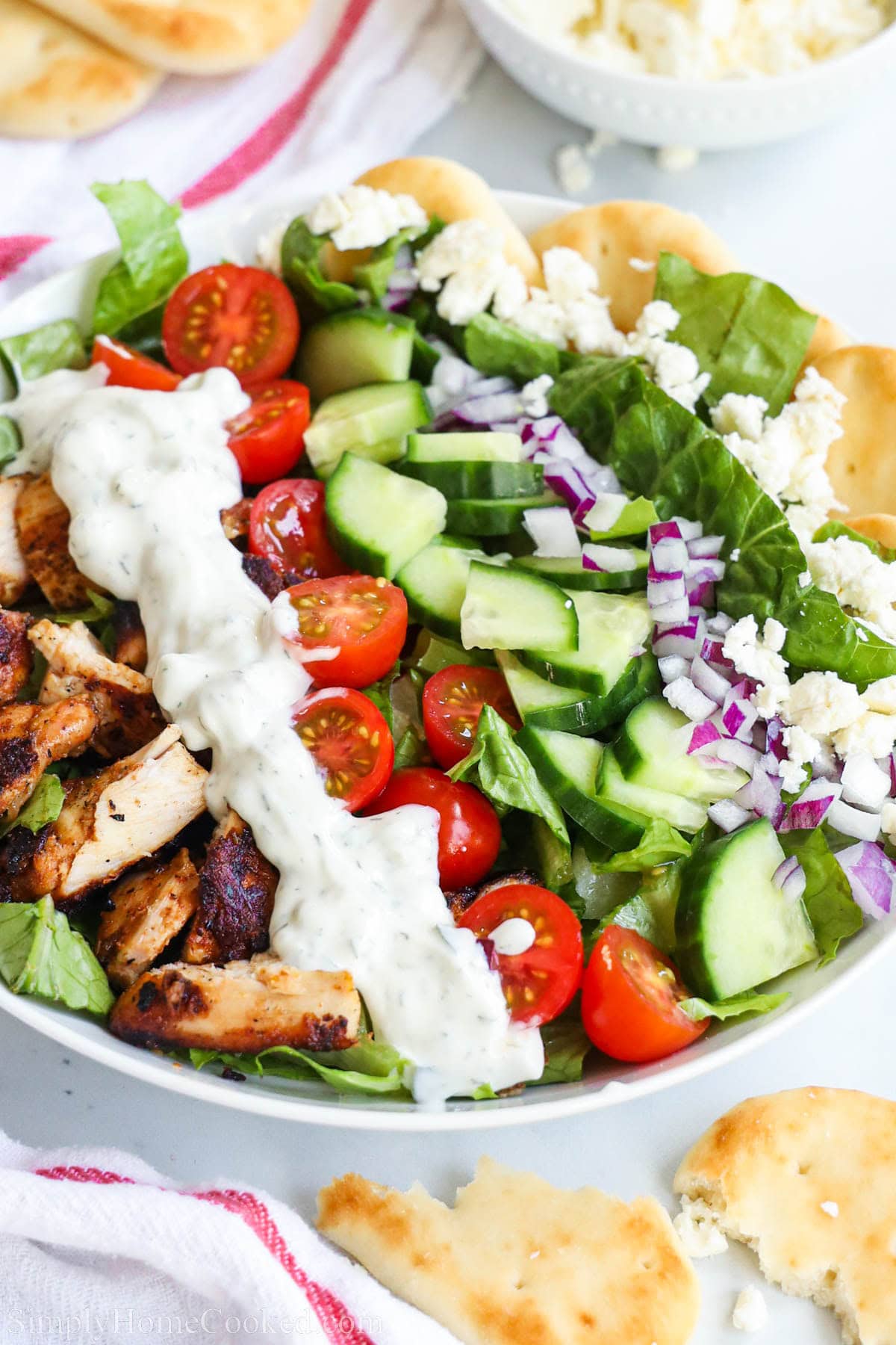Close up of Chicken Shawarma bowl with tzatziki sauce, tomatoes, cucumbers, onion, feta cheese, and pita bread.