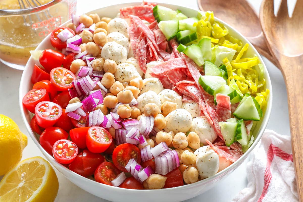 Chopped Italian Salad with lemons and salad tossing utensils nearby.