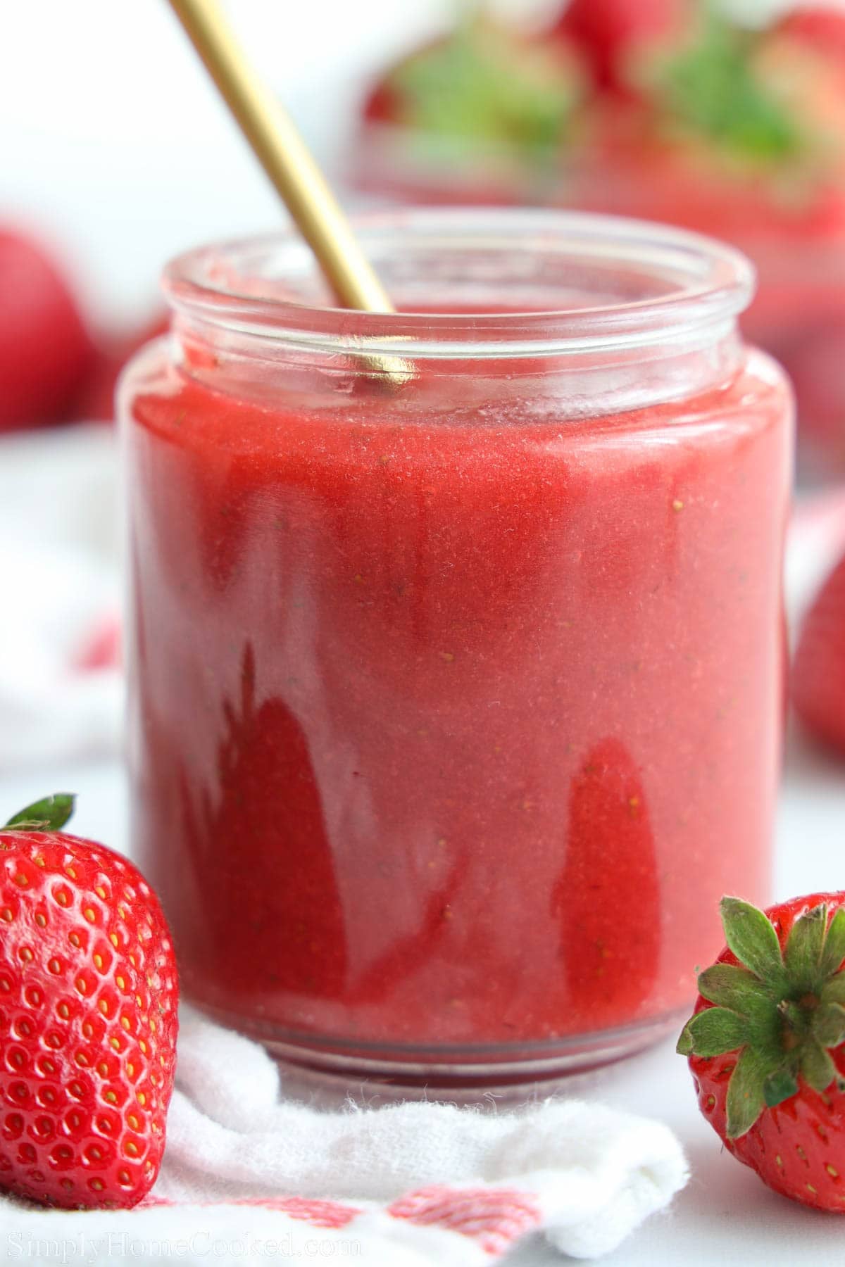Strawberry Puree in a jar with a spoon in it and strawberries nearby.